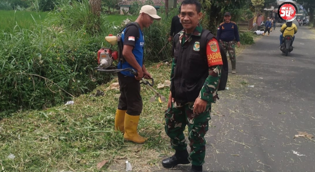 Babinsa Kadudampit Koramil 09/Cisaat Gelar Kerja Bakti Pembersihan Rumput Liar di Bahu Jalan
